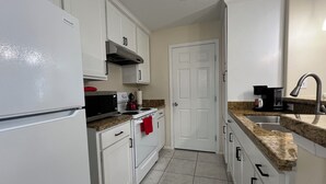 Una cocina compacta con gabinetes blancos, un lavamanos de acero inoxidable y un microondas.