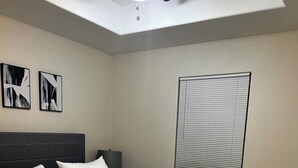 Un dormitorio con una cama, una mesita de noche, un ventilador de techo y una ventana con persianas.