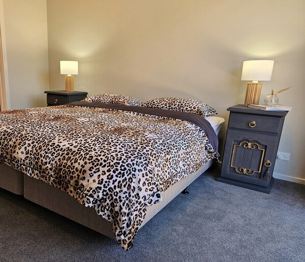 Une chambre à coucher avec un grand lit, deux tables de chevet avec des lampes et une petite commode sombre dotée d’une porte décorative.