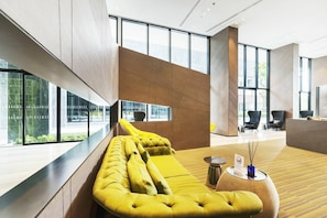 A modern lobby with a yellow sofa, large windows, and a reception desk. - Great Location With Infinity Pool -central Pattaya (Pattaya)