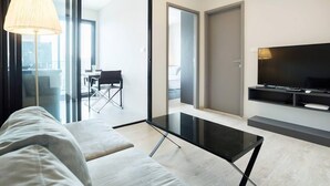 Un salon moderne avec une table basse en verre, un canapé, un téléviseur et une lampe.