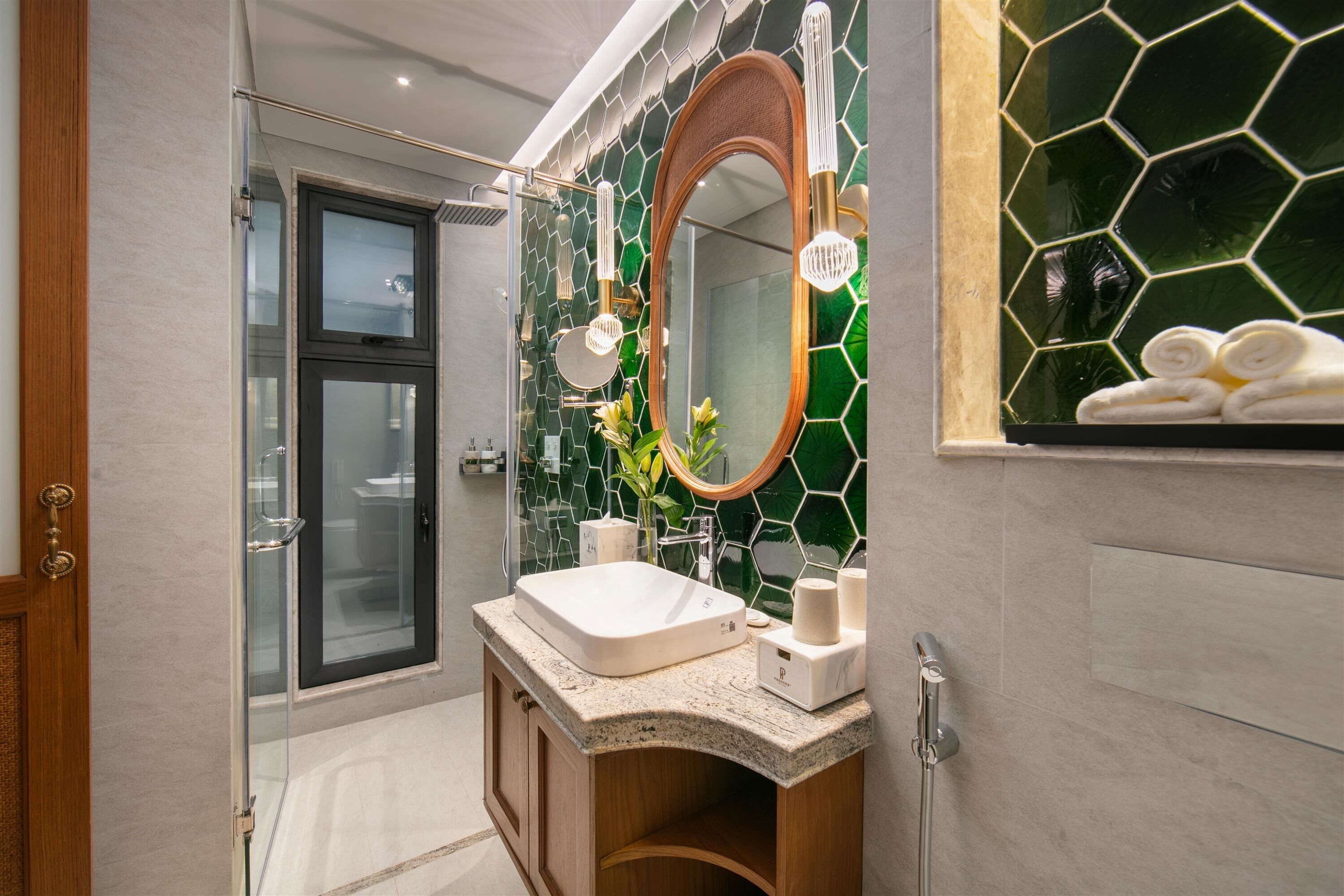 A modern bathroom with a glass shower enclosure, a freestanding sink, and a mirror with a hexagonal tile backsplash.