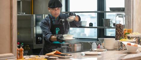 A chef preparing food in a kitchen with stainless steel appliances and a large window.