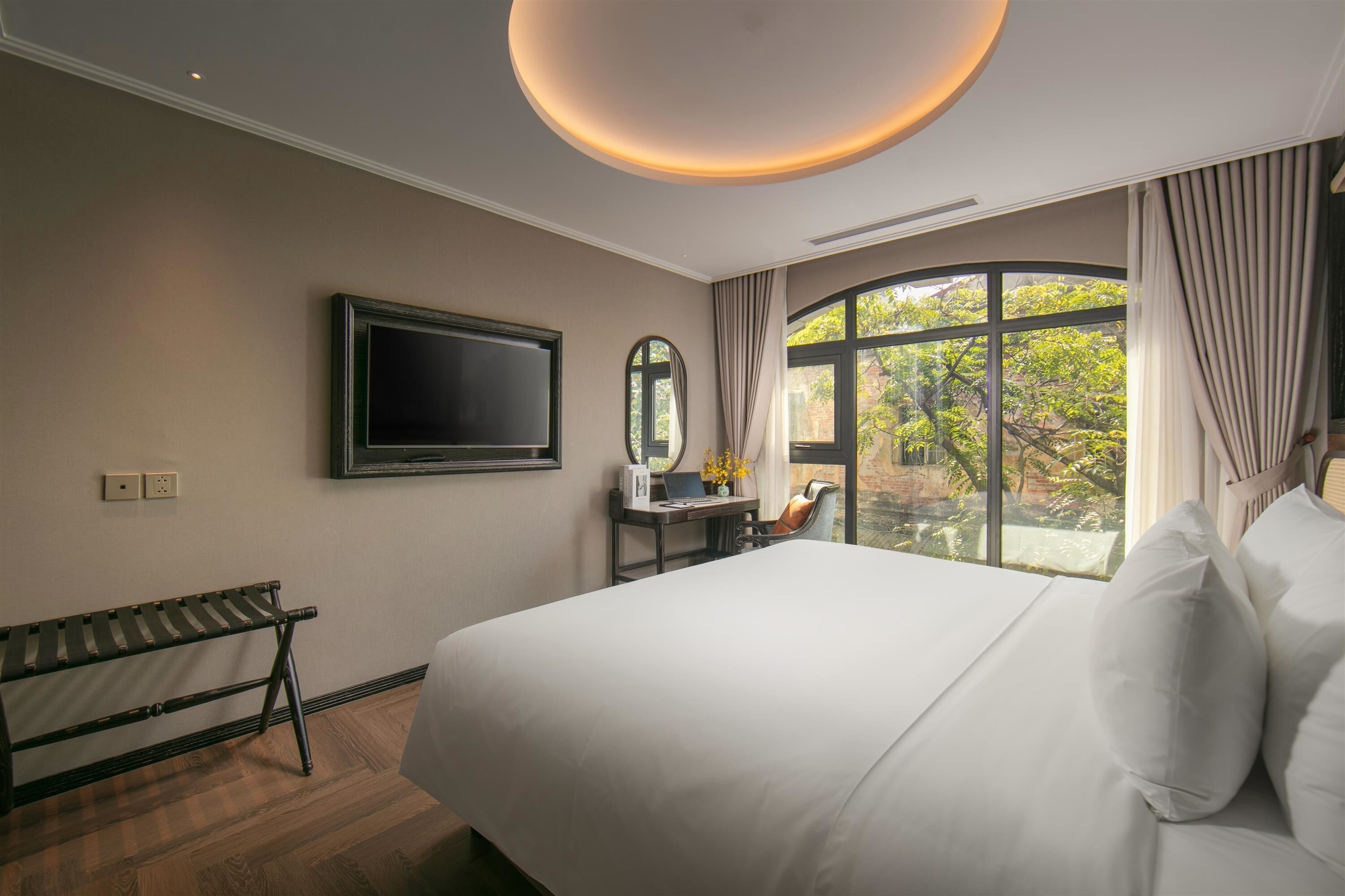 A hotel room with a large bed, a desk with a laptop, a television, and a window with curtains.
