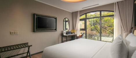 A hotel room with a large bed, a desk with a laptop, a television, and a window with curtains.
