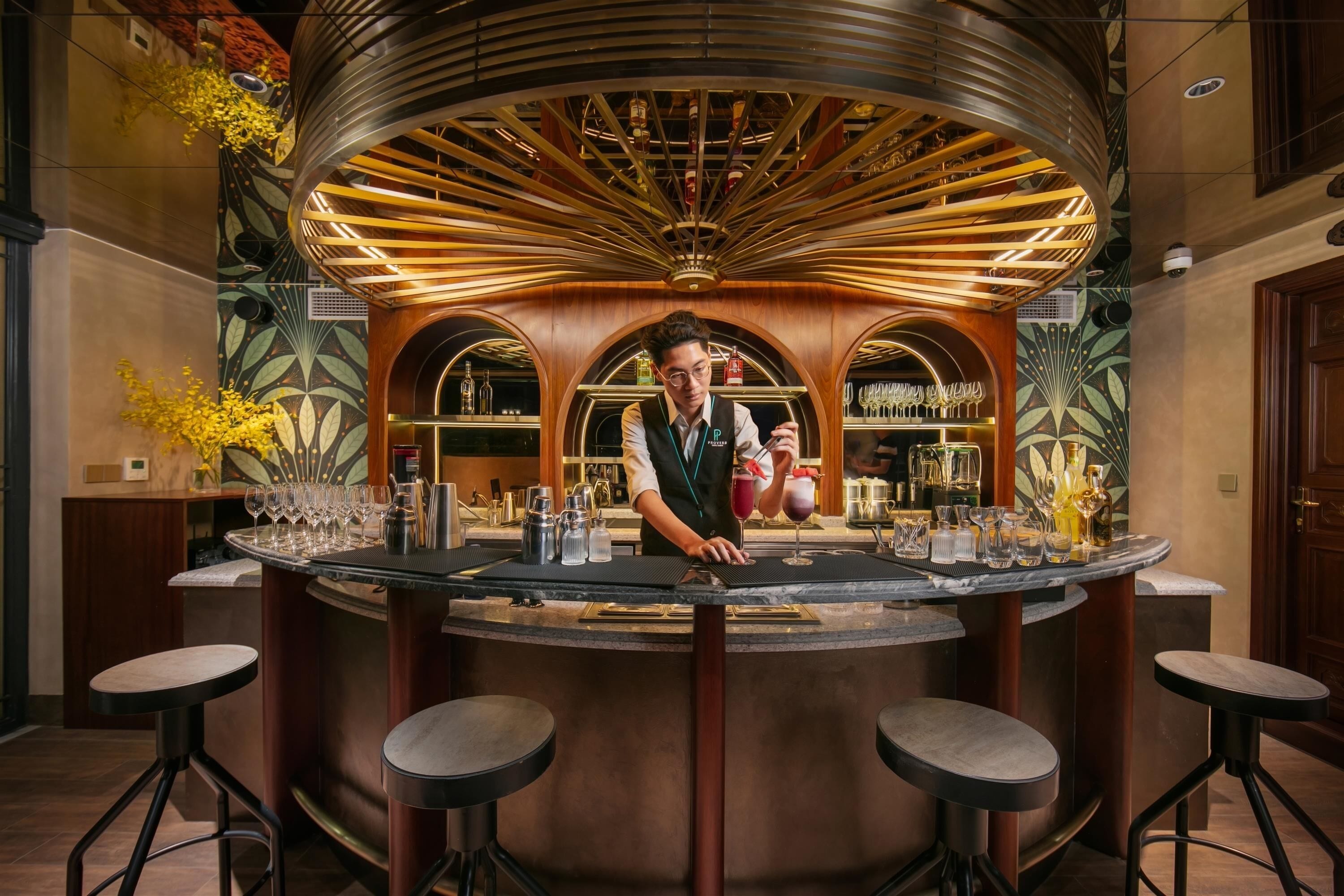 A bar area with a bartender, a circular bar counter, and stools. There are shelves with bottles and glasses in the background.