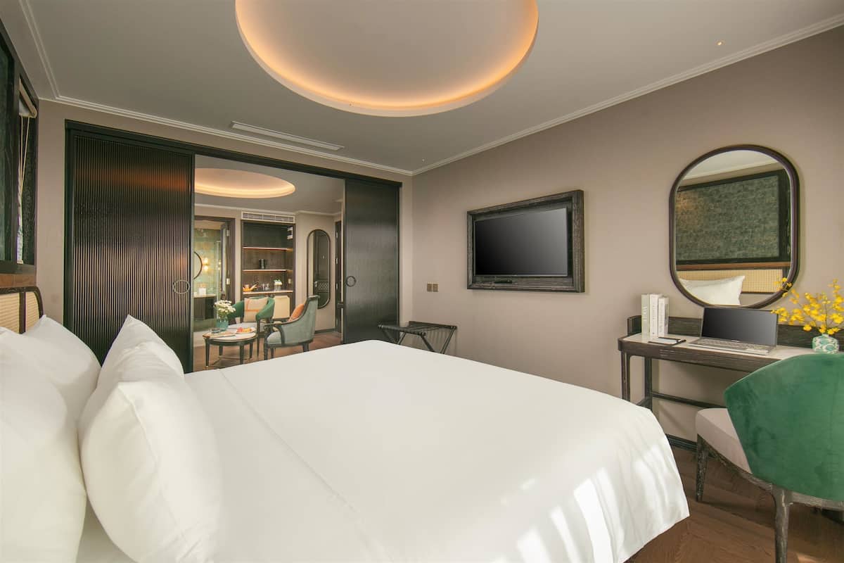 Una habitació d'hotel amb un llit gran, un escriptori amb un ordinador, un mirall i una televisió penjada a la paret.