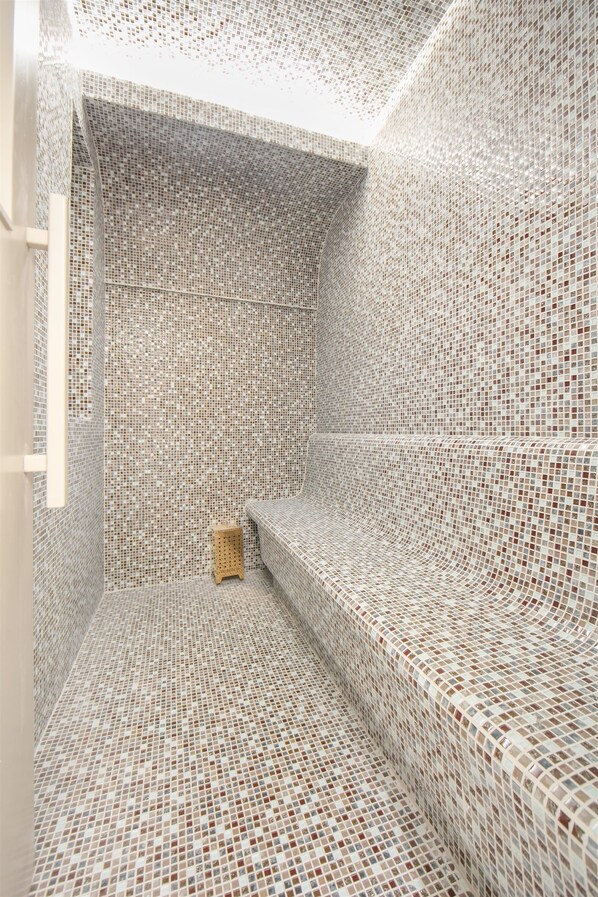 Una habitación con paredes y suelo de mosaico, un banco de madera y un taburete pequeño.
