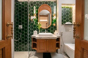 Un baño con salpicadero de azulejos hexagonales verdes, un mueble de tocador de madera con un lavabo, un espejo y una bañera.