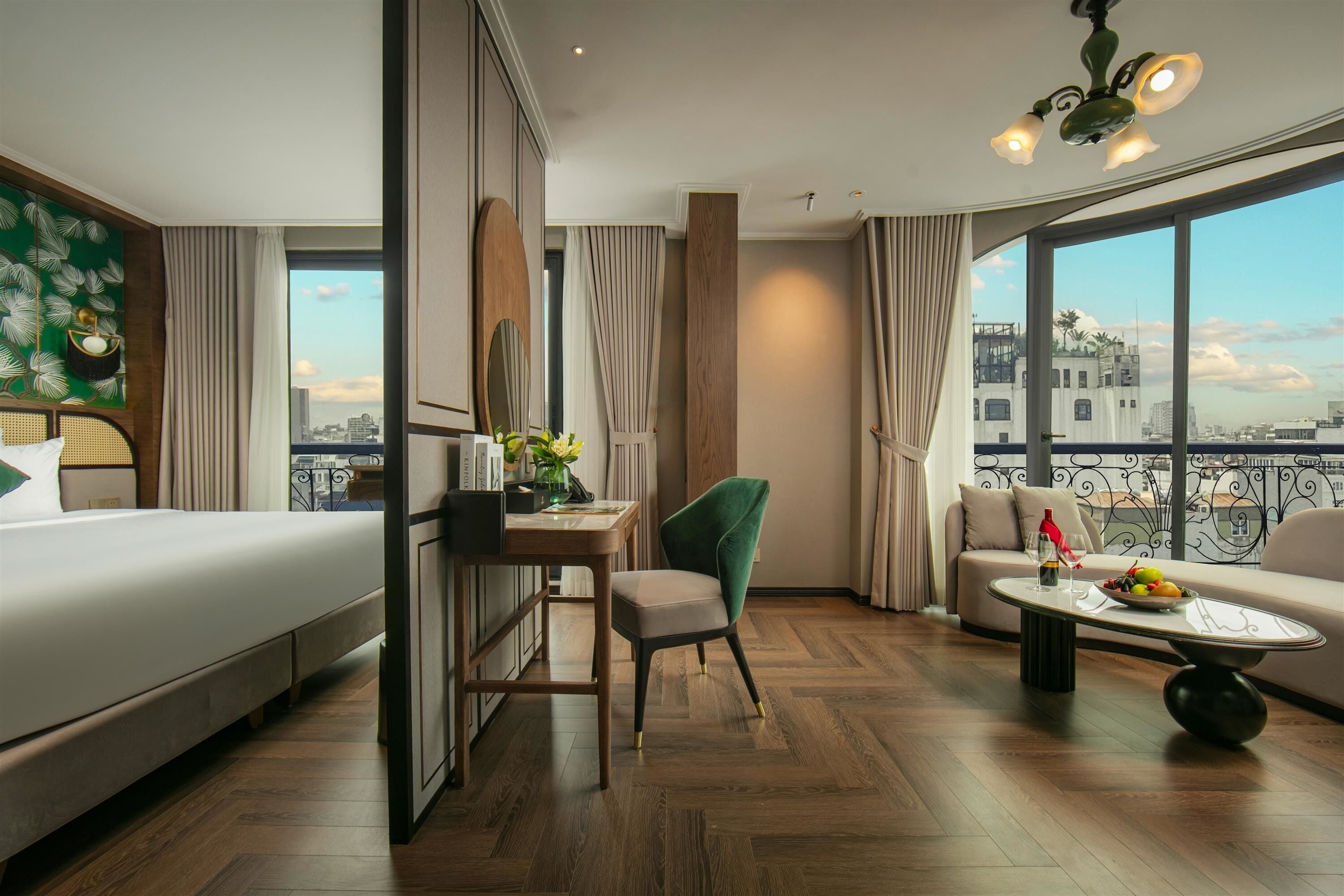 Ein Hotelzimmer mit Bett, Schreibtisch, Stuhl, Sofa und einem Balkon mit Blick auf die Stadt.