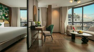 Een hotelkamer met een bed, bureau, stoel, bank en een balkon met uitzicht op de stad.