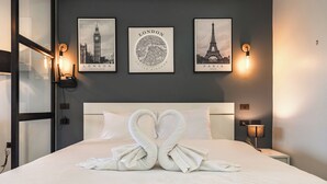 Une chambre d’hôtel avec un lit soigneusement fait, deux appliques murales et trois tableaux représentant des monuments célèbres.