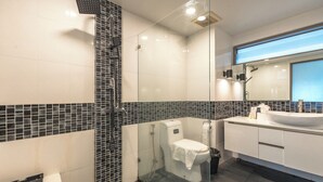 Une salle de bain moderne avec une douche à parois de verre, des toilettes blanches et un grand lavabo surmonté d’un miroir.