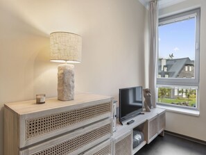 A modern living room with a TV on a wooden console, a stone lamp, and a view of a house through a large window.
