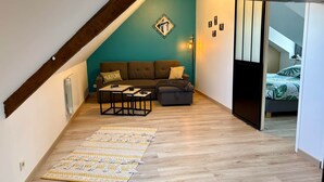 A cozy loft bedroom with a sloped ceiling, a brown sofa, a small coffee table, and a patterned rug on the wooden floor. - Welcome to Marie & Guillaume's 2* rated home (Carentan-les-Marais)