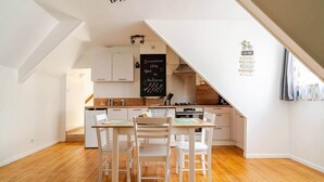 A modern kitchen with white cabinetry, a chalkboard menu, and a dining area with a wooden table and white chairs. - Welcome to Marie & Guillaume's 2* rated home (Carentan-les-Marais)