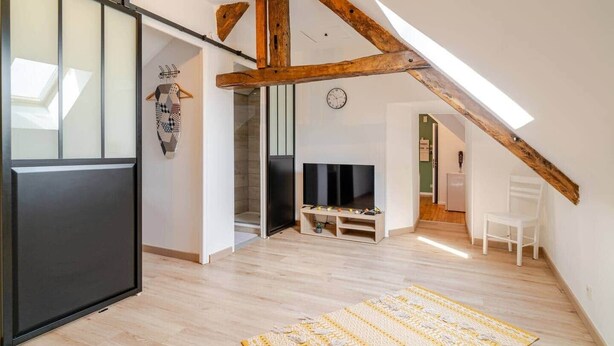 A loft-style room with exposed wooden beams, a sliding door, a flat-screen TV, and a patterned rug. - Welcome to Marie & Guillaume's 2* rated home (Carentan-les-Marais)