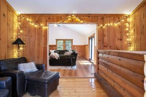 Interior acogedor de una cabaña de troncos, con piso de madera, un sofá de cuero negro y un banco de madera.