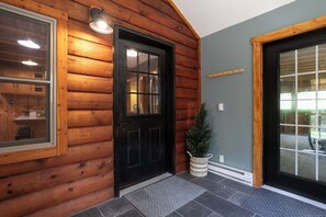 Fachada de madera con una puerta negra, una pequeña planta en maceta y una ventana con una lámpara.