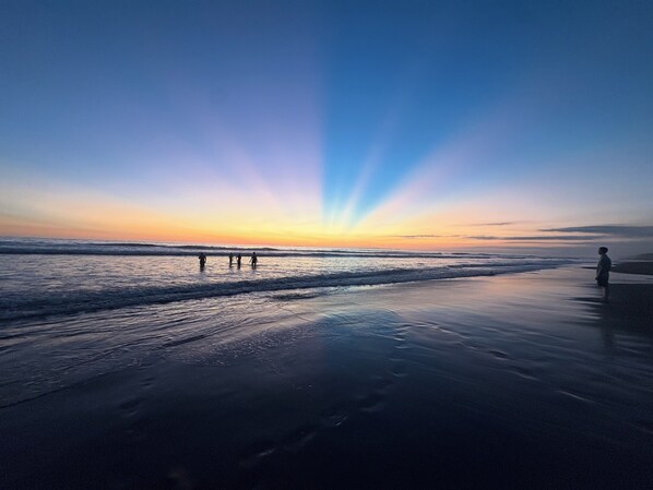 Uma praia com um pôr do sol, águas calmas e um cais.