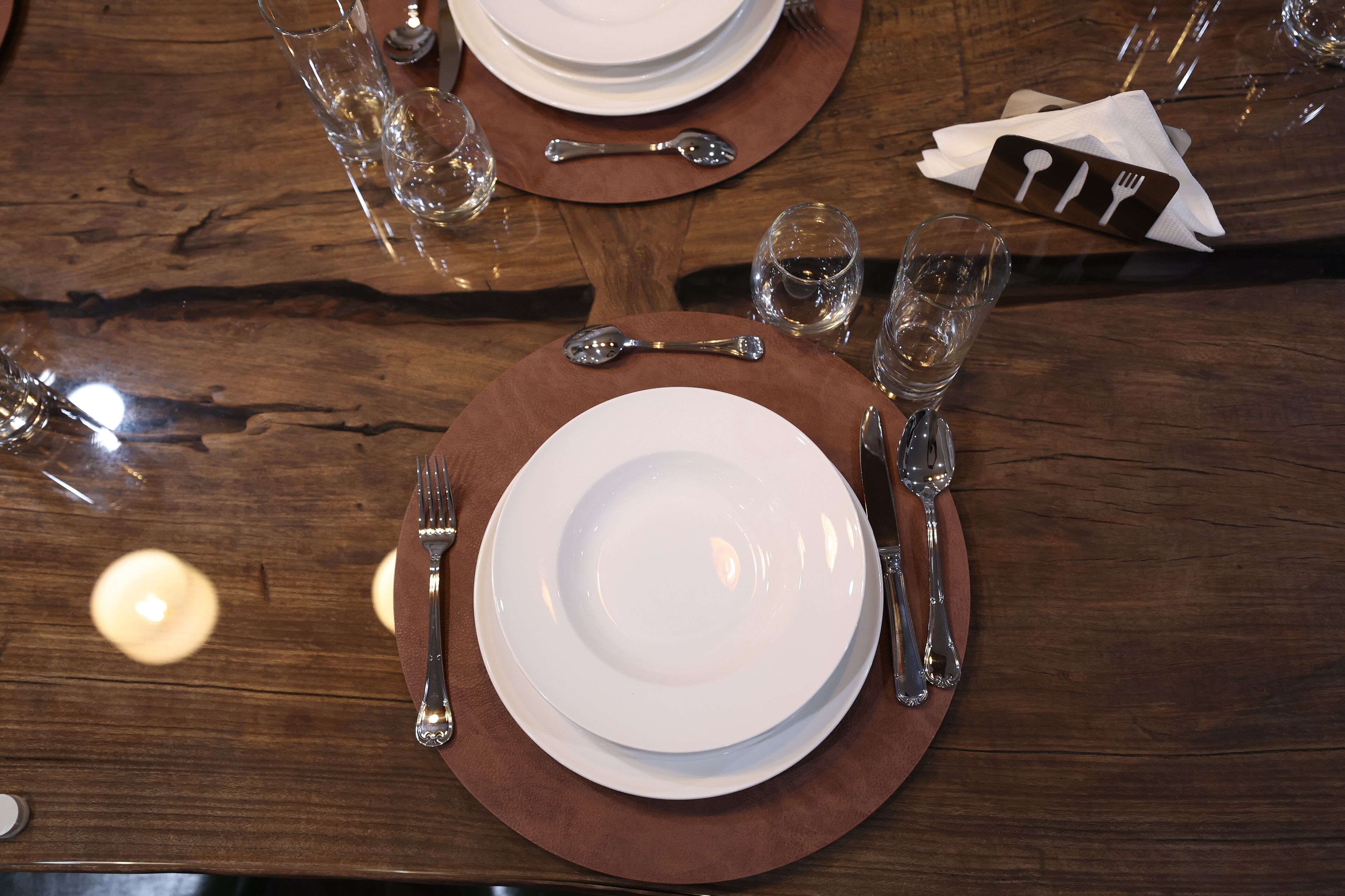 Une table de salle à manger en bois, mise avec des assiettes, des couverts et des verres.