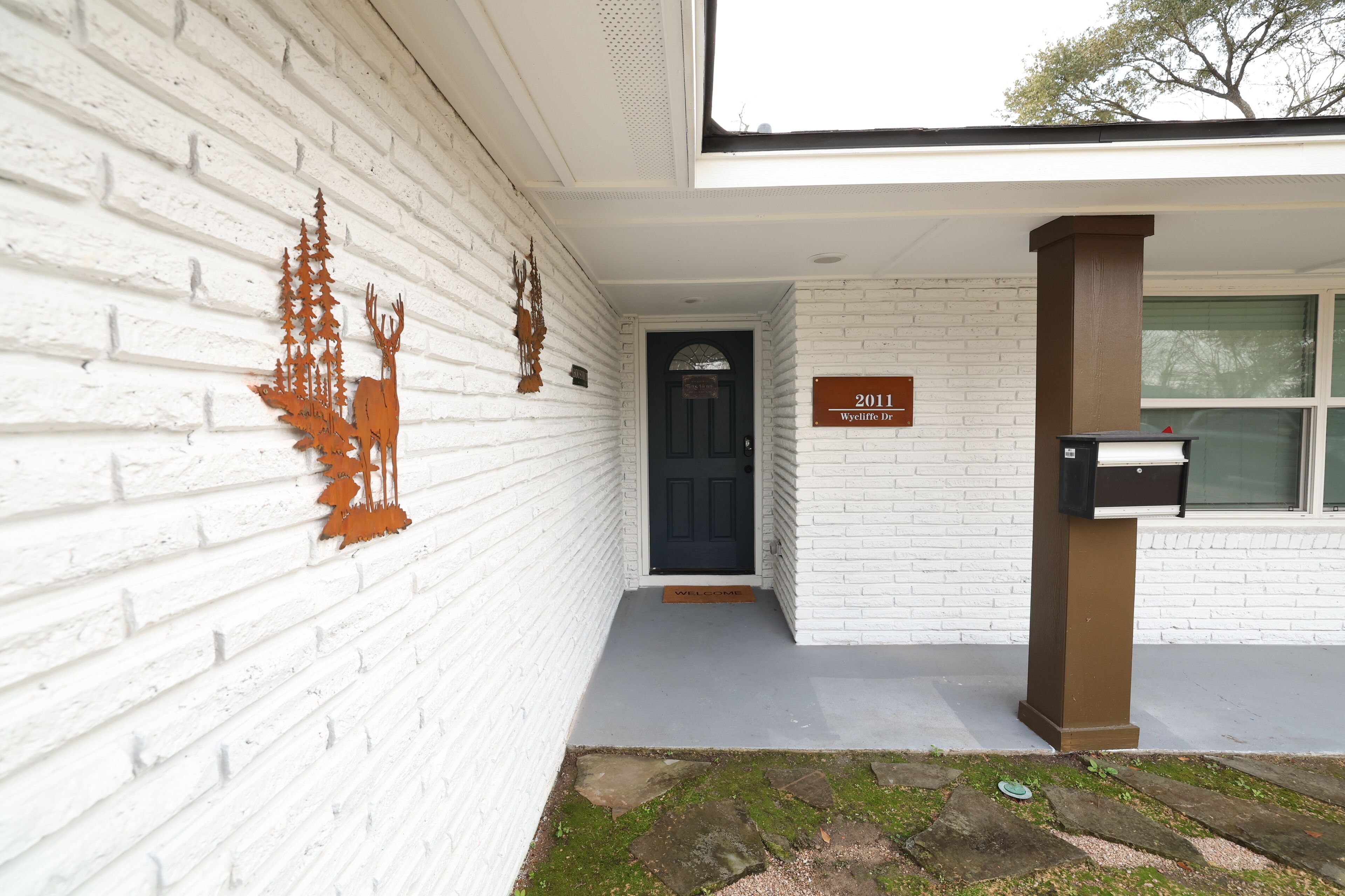 A white brick building with a black door, a mailbox, and a welcome mat.