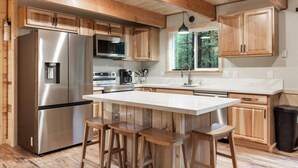 A modern kitchen with wooden cabinets, stainless steel appliances, and a large island with bar stools. - Barratt Lodge | Hot Tub | 35 mins to Yellowstone (Island Park)