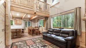 A cozy cabin interior with a dining area, a sofa, and a staircase leading to an upper level. - Barratt Lodge | Hot Tub | 35 mins to Yellowstone (Island Park)