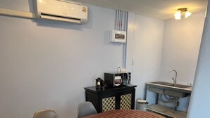 A conference room with a wooden table and grey chairs, an air conditioning unit, a small kitchenette, and a sink. - Baan saen saran residence (แขวงคลองชักพระ เขตตลิ่งชัน)