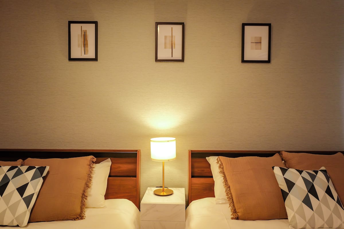 Habitación de hotel con dos camas, una mesita de noche con lámpara y tres cuadros enmarcados en la pared.
