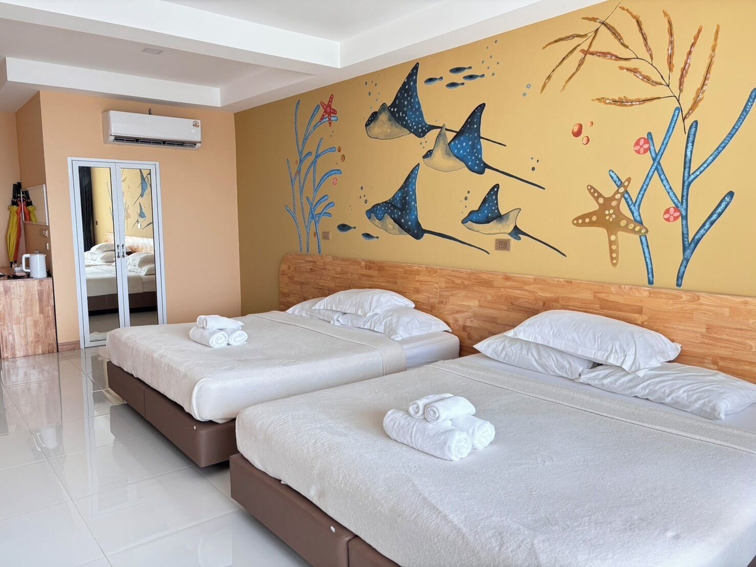 Una habitación de hotel con dos camas, cabecero de madera, un mural en la pared y un espejo.