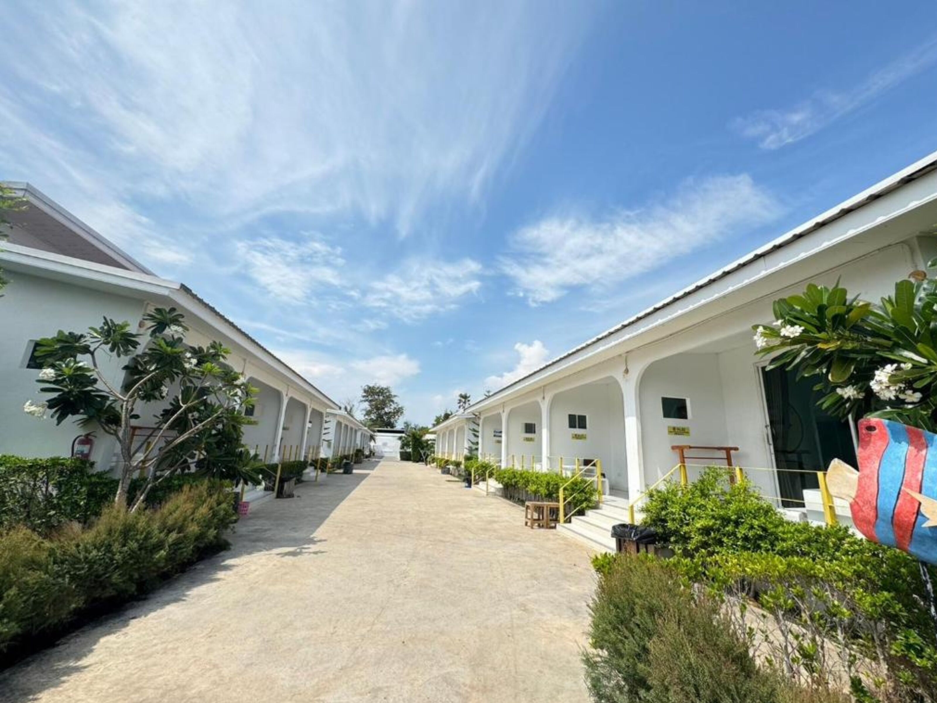 A row of white buildings with a central pathway, surrounded by greenery and a clear sky.