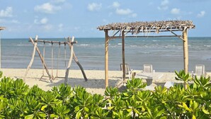 Une plage agrémentée de structures en bois, notamment une aire de jeux avec des balançoires et un espace abrité avec des chaises.