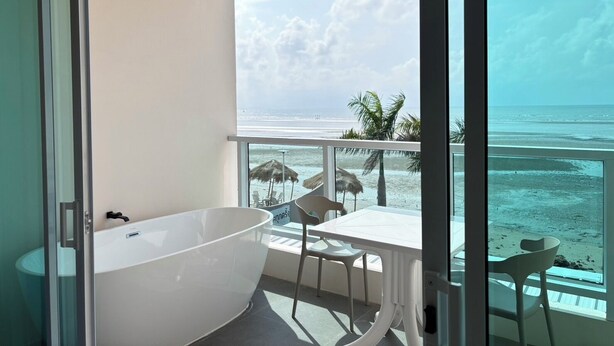 Un balcon avec vue sur la plage, une baignoire et deux chaises.