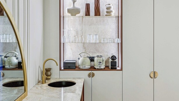 A bathroom with a marble sink, a gold faucet, and a mirror. There is a shelf above the sink with various glassware and a white kettle. - Modern Apartment - 2P - Parc Monceau (Paris)