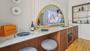 A modern kitchen with a marble countertop, wooden cabinets, and a built-in oven. There are two bar stools and a Louis Vuitton bag on the counter. - Modern Apartment - 2P - Parc Monceau (Paris)