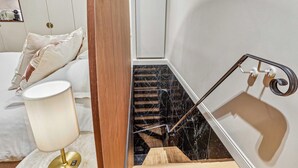 A modern hotel room with a wooden floor, a white bed with pillows, a bedside lamp, a marble staircase, and a large mirror. - Modern Apartment - 2P - Parc Monceau (Paris)