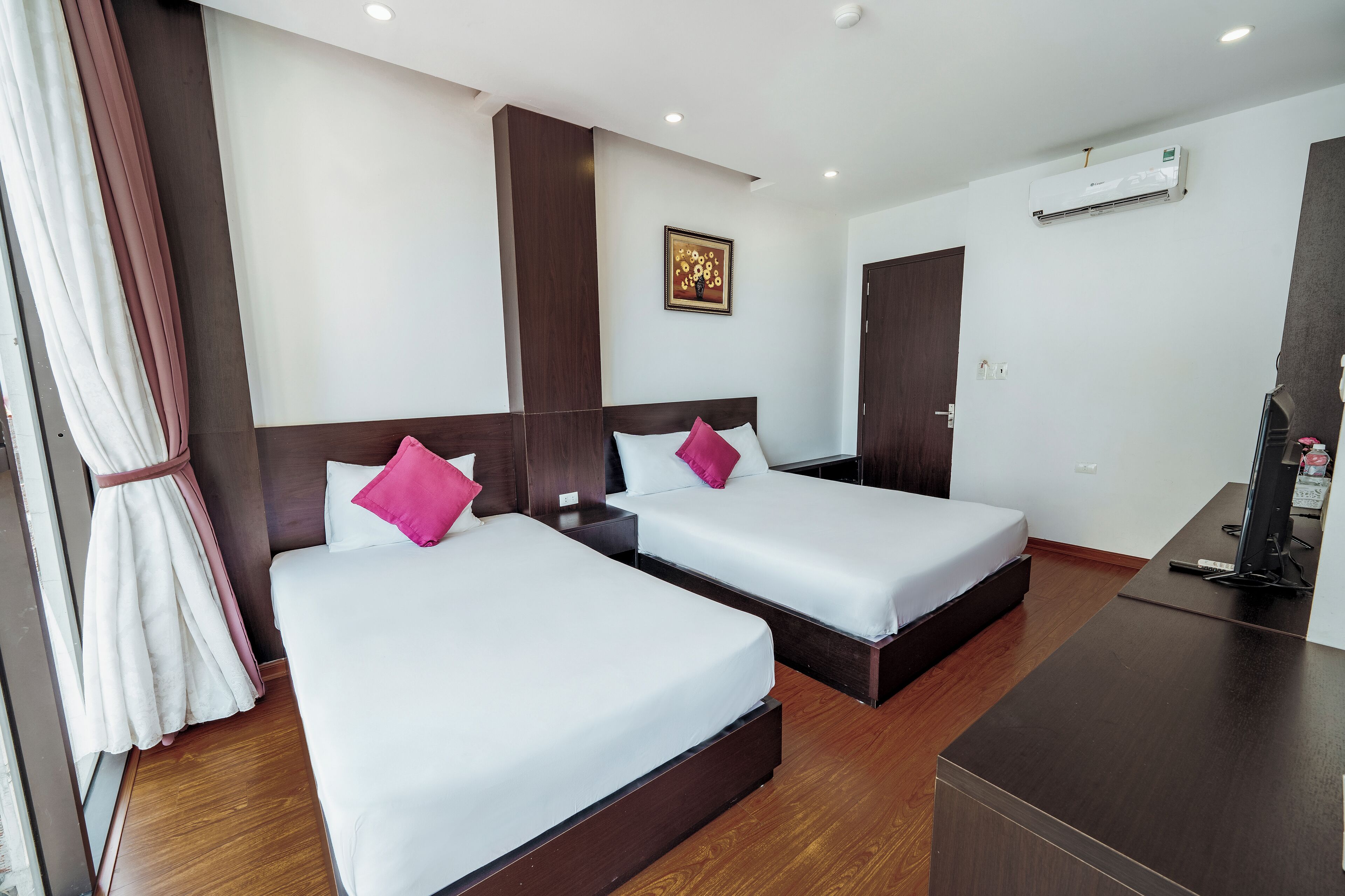 Quarto de hotel com duas camas, uma escrivaninha, ar condicionado e um quadro na parede.