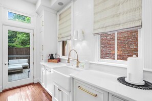 A kitchen with white cabinetry, a large window with a view of a brick wall and greenery, and a built-in sink with a gold faucet.