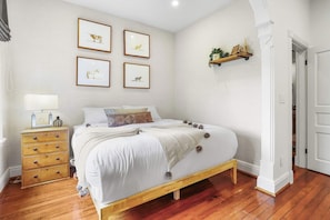 A bedroom with a wooden bed, white bedding, a nightstand with a lamp, and framed animal pictures on the wall.