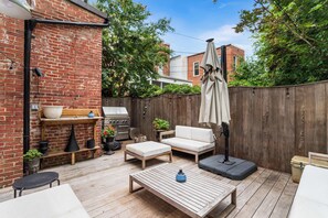 A wooden deck with outdoor furniture, a grill, and a brick wall.