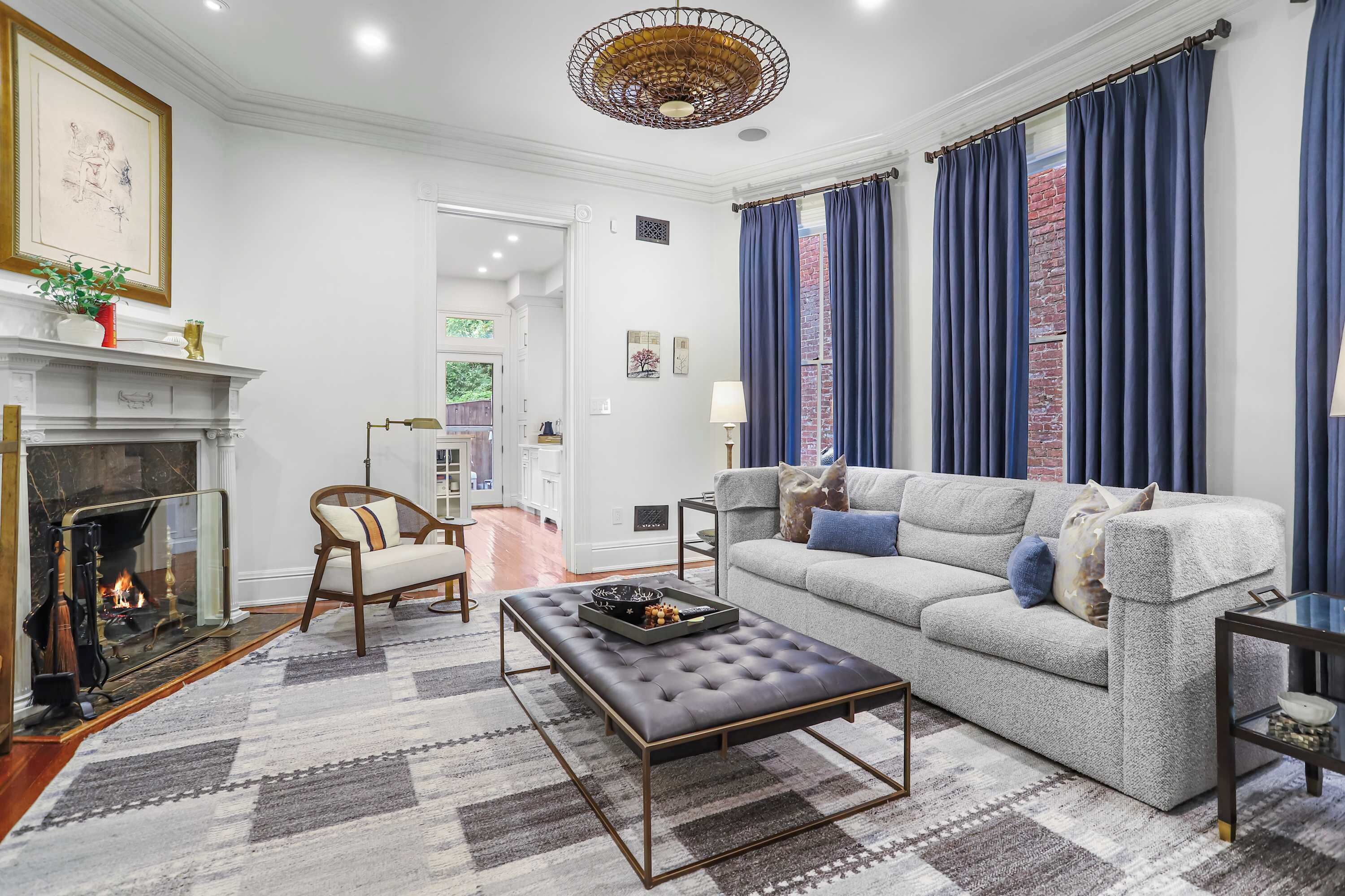 A living room with a fireplace, a sofa, a coffee table, and a view of a brick wall through blue curtains.