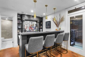Una cucina moderna con angolo bar, caratterizzata da un piano di lavoro nero, tre sgabelli da bar grigi e lampade a sospensione dorate.