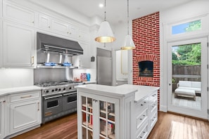 A modern kitchen with white cabinetry, stainless steel appliances, and a brick accent wall.