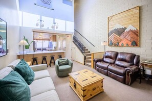 A spacious living area with a sofa, a coffee table, and a leather couch. A staircase is visible in the background leading to an upper level.