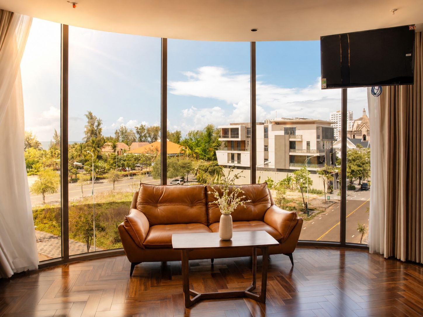 A room with a leather sofa, a wooden coffee table, and a large window offering a view of buildings and greenery.