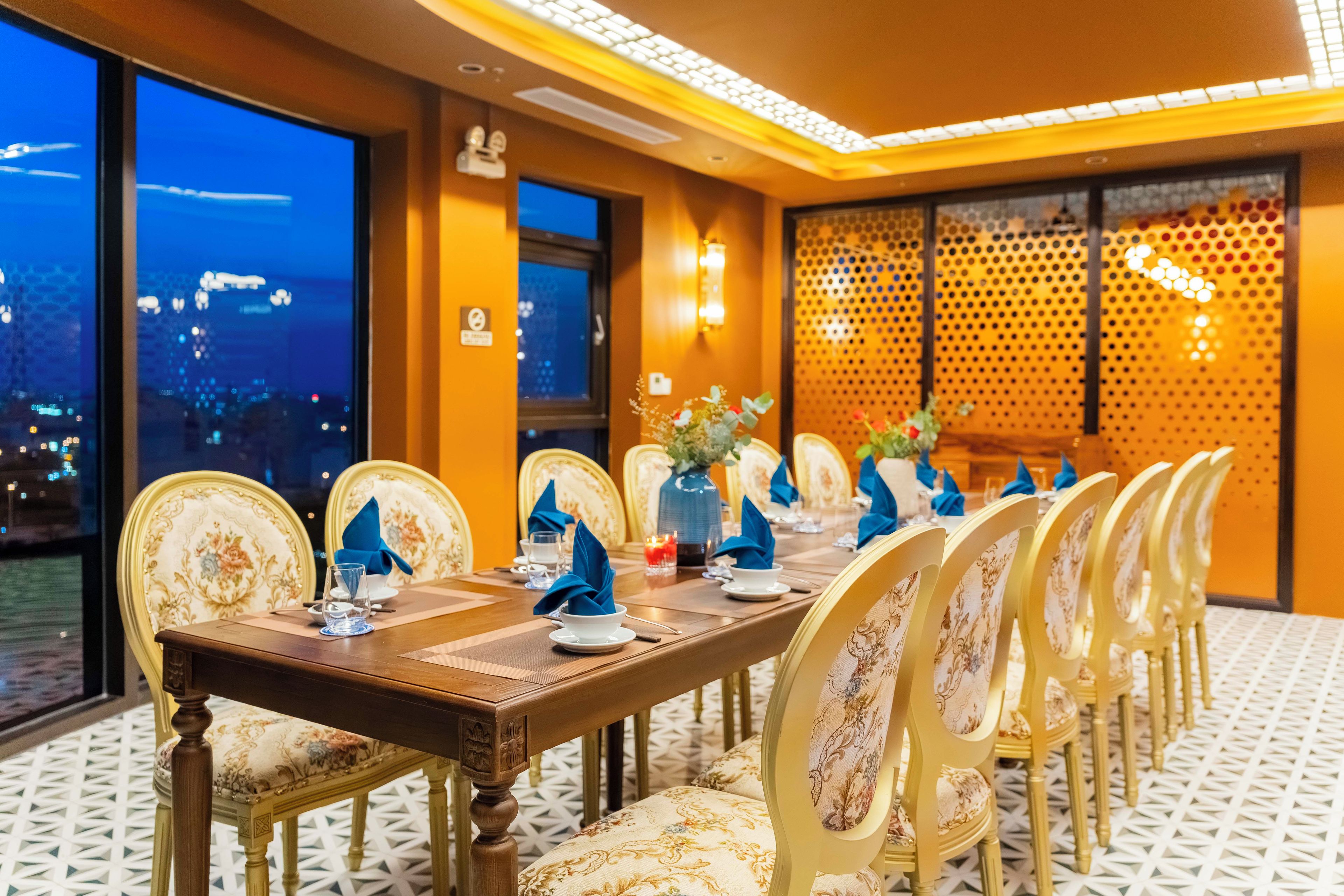 Comedor con una mesa larga dispuesta para varios invitados, con sillas ornamentadas y vistas de la ciudad a través de amplias ventanas.