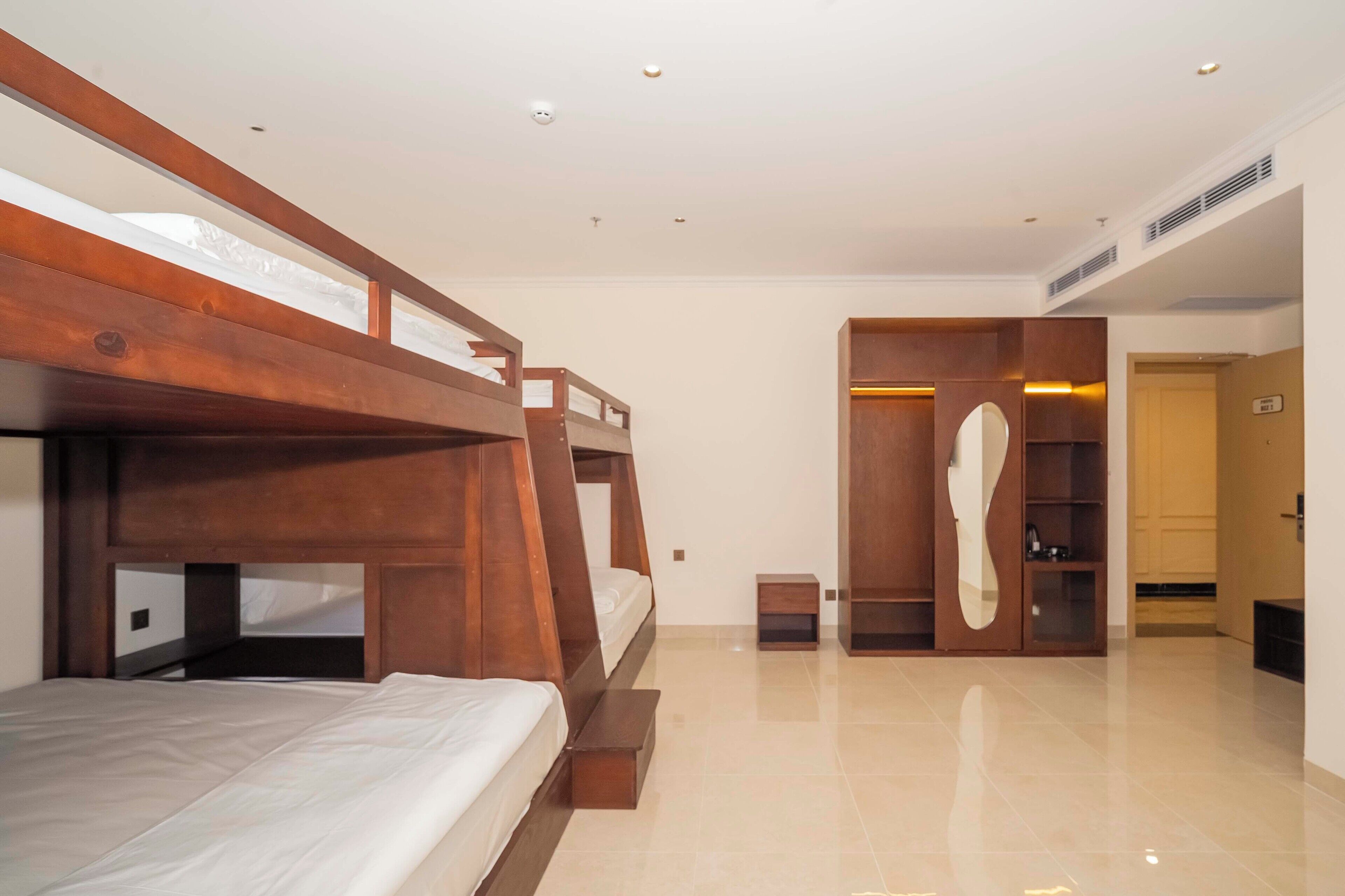 Habitación de hotel con literas, un armario de madera, una mesita de noche pequeña y un espejo.