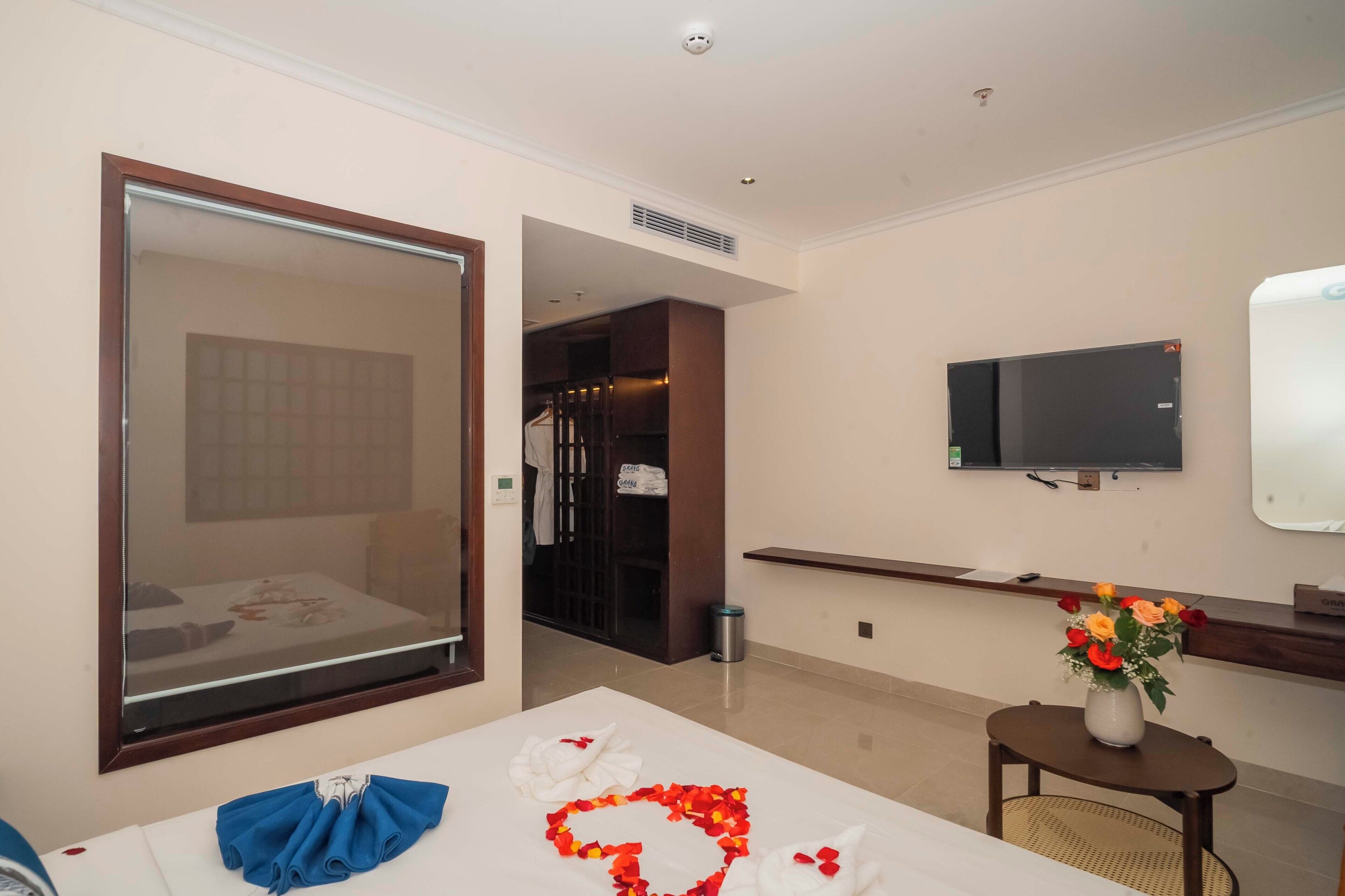 Een hotelkamer met een bed, een aan de muur bevestigde televisie, een tafeltje met een bloevas en een raam met uitzicht.