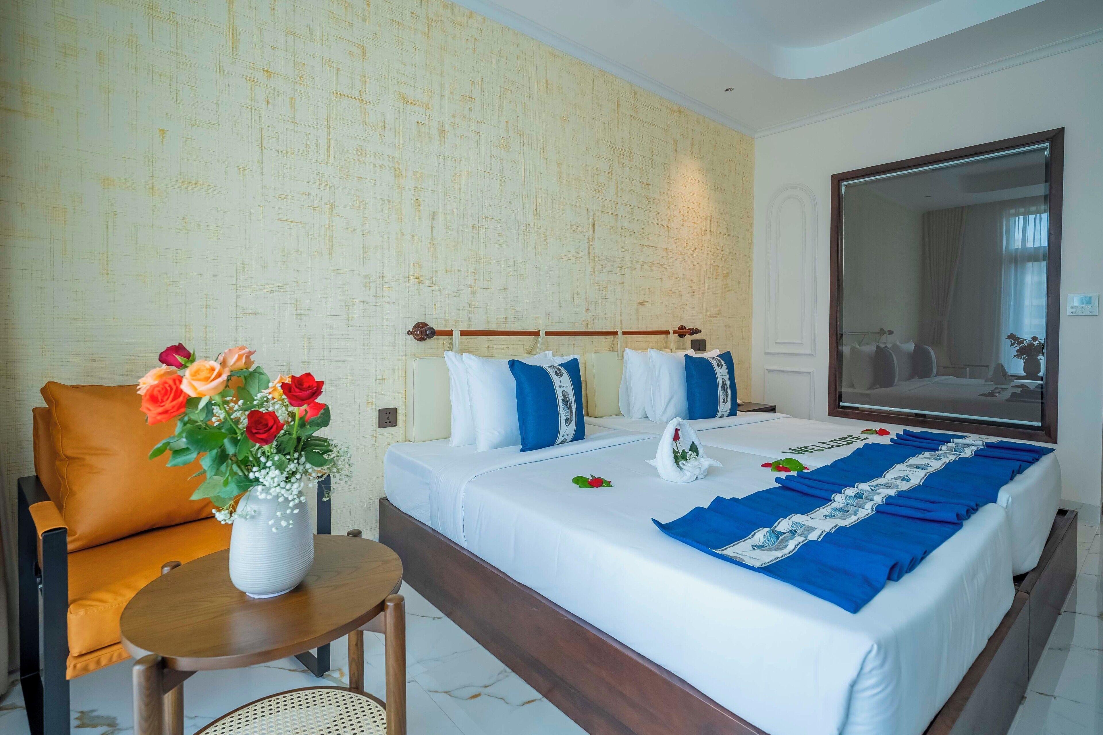 A hotel room with a large bed, a wooden headboard, a small table with a vase of flowers, and a large mirror on the wall.